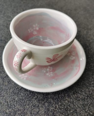 Kleine Tasse mit Untertasse, blassrosa und floralem Muster.